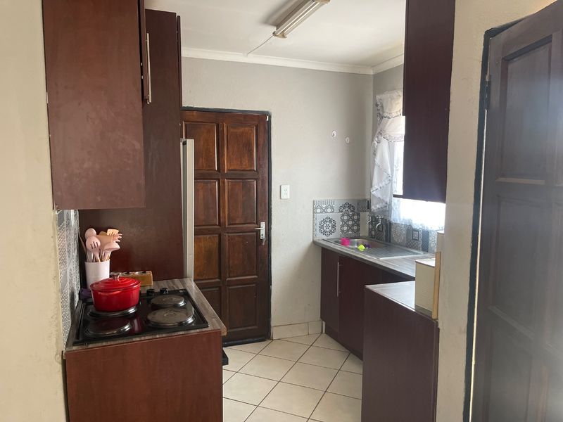 A functional kitchen featuring dark wood cabinetry, an electric hob, tiled flooring, and a patterned tile backsplash with direct access to an exterior door.