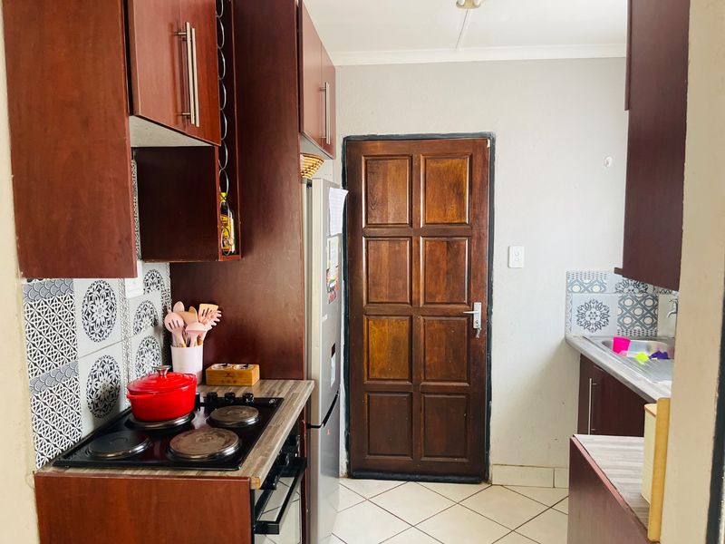 A functional kitchen featuring dark wood cabinetry, a built-in electric hob and oven, patterned tiled backsplash, and tiled flooring.
