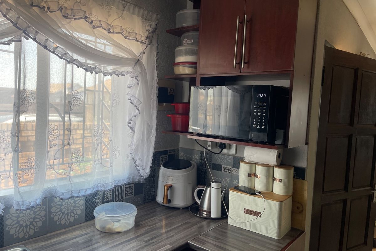 A functional kitchen corner featuring laminate countertops, patterned wall tiling, and built-in cabinetry with a dedicated microwave shelf.