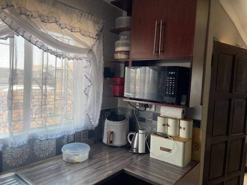 A functional kitchen corner featuring laminate countertops, patterned wall tiling, and built-in cabinetry with a dedicated microwave shelf.