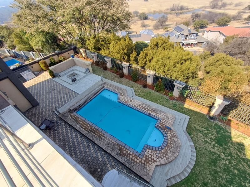 Elevated view of a backyard featuring a swimming pool, paved patio area, and a built-in fire pit, overlooking the surrounding landscape.