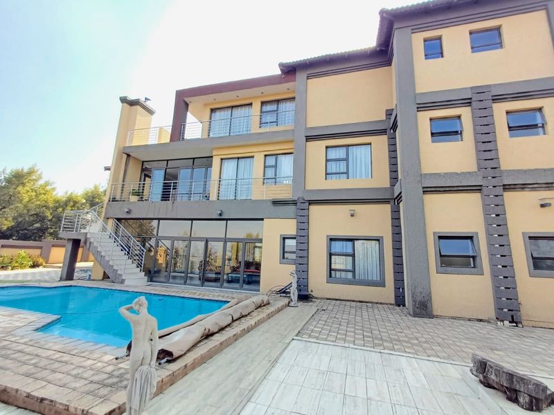 Rear elevation of a multi-story house featuring a swimming pool, paved patio area, multiple balconies, and large glass sliding doors.