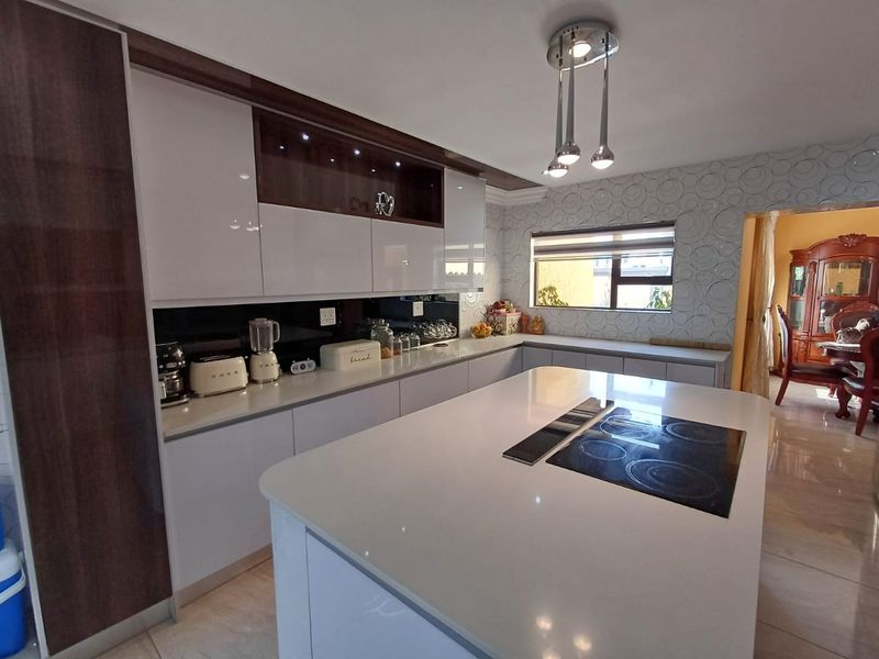 Modern kitchen featuring a central island with an integrated electric hob, sleek cabinetry, stone countertops, and stylish decorative wall tiling.