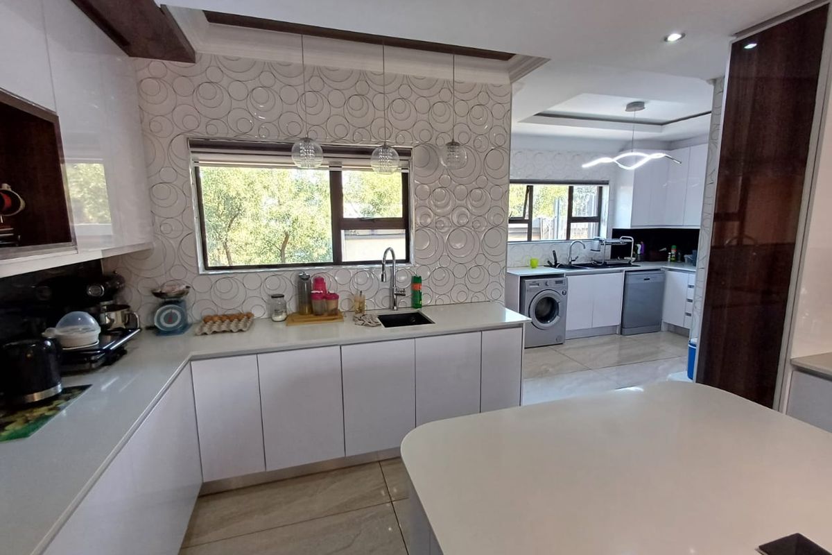 Modern, well-appointed kitchen featuring high-gloss cabinetry, quartz countertops, a decorative tiled backsplash, and integrated laundry facilities in an open-plan layout.