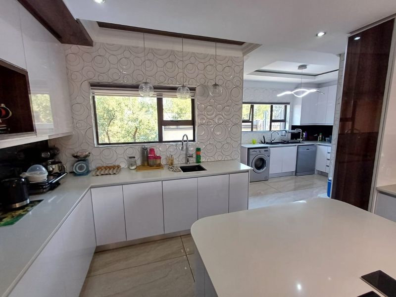 Modern, well-appointed kitchen featuring high-gloss cabinetry, quartz countertops, a decorative tiled backsplash, and integrated laundry facilities in an open-plan layout.