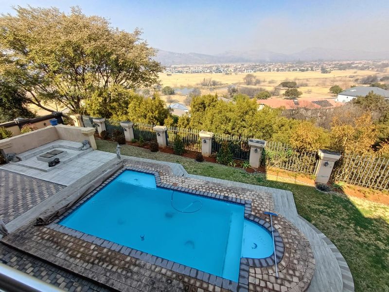 An elevated view of a swimming pool with a paved surround, raised patio area, and metal fencing overlooking a scenic landscape.