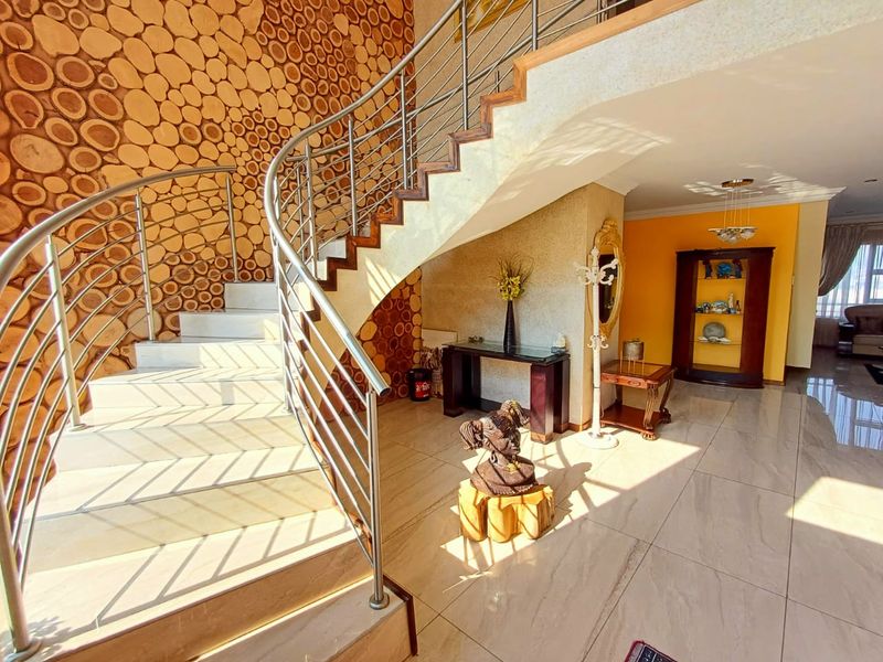 Spacious entrance hall featuring a striking curved staircase with stainless steel balustrades and a unique wood log feature wall.
