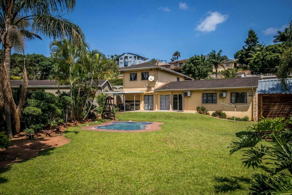Rear view of the property featuring a spacious lawn, a swimming pool, and a two-story residential structure with tiled roofing.