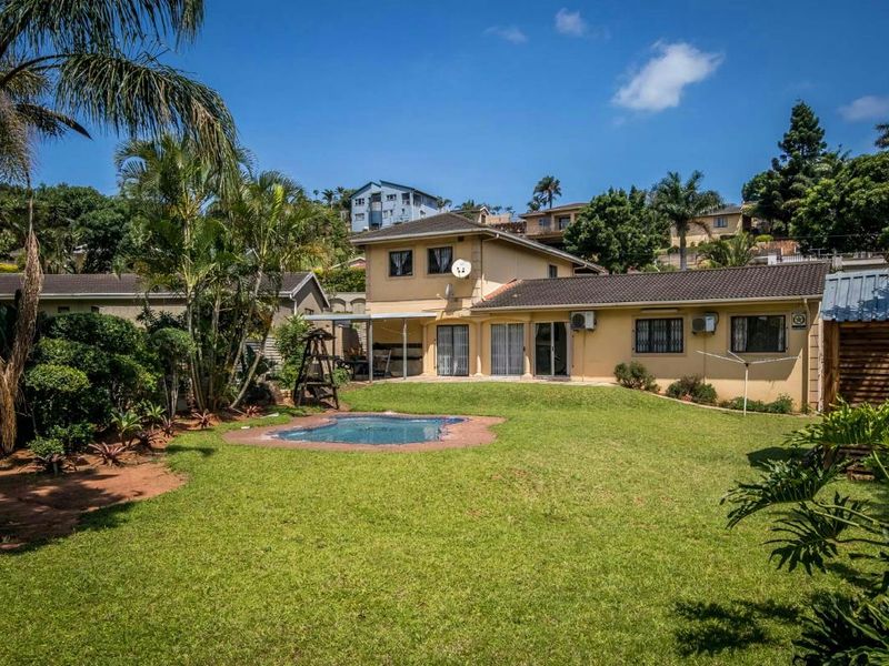 Rear view of the property featuring a spacious lawn, a swimming pool, and a two-story residential structure with tiled roofing.