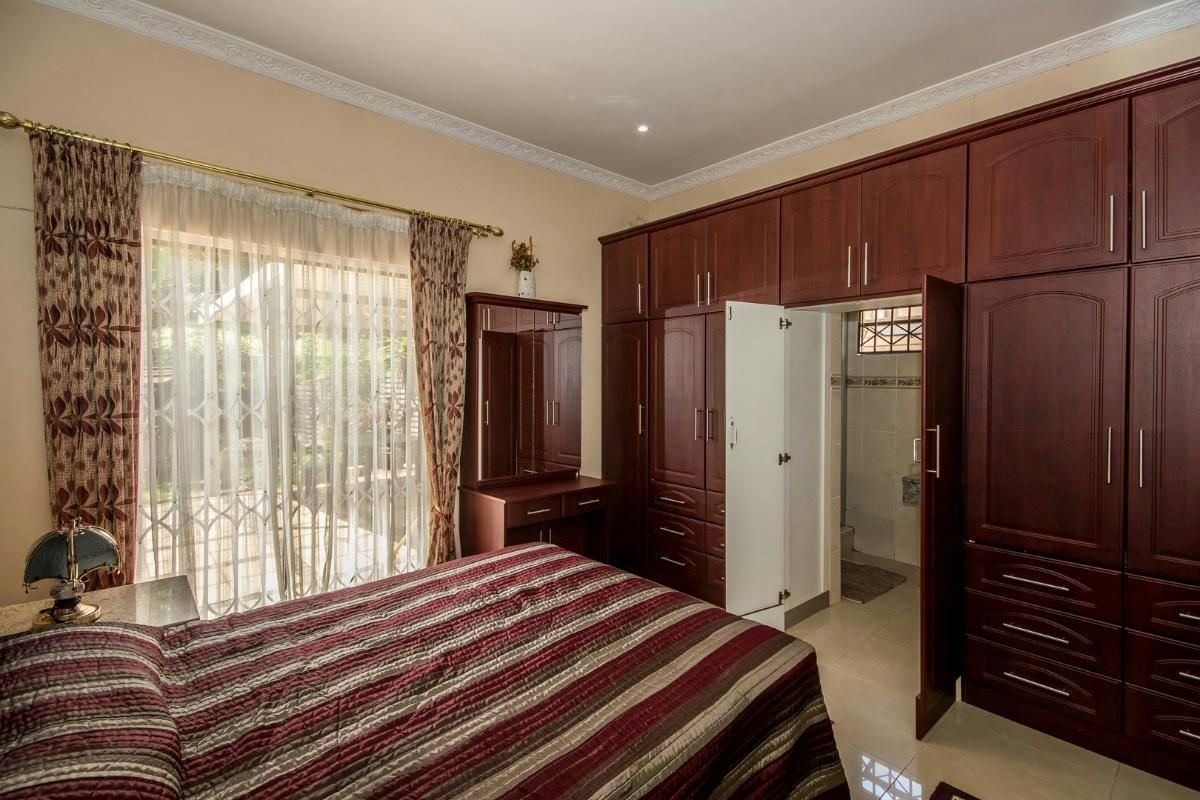 A well-maintained bedroom featuring extensive built-in wooden cabinetry, tiled flooring, and direct access to an outdoor patio through sliding glass doors.