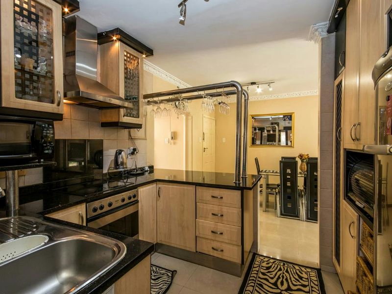 A functional kitchen featuring light wood cabinetry, black granite countertops, stainless steel appliances, and a breakfast bar, leading into an adjacent dining area.