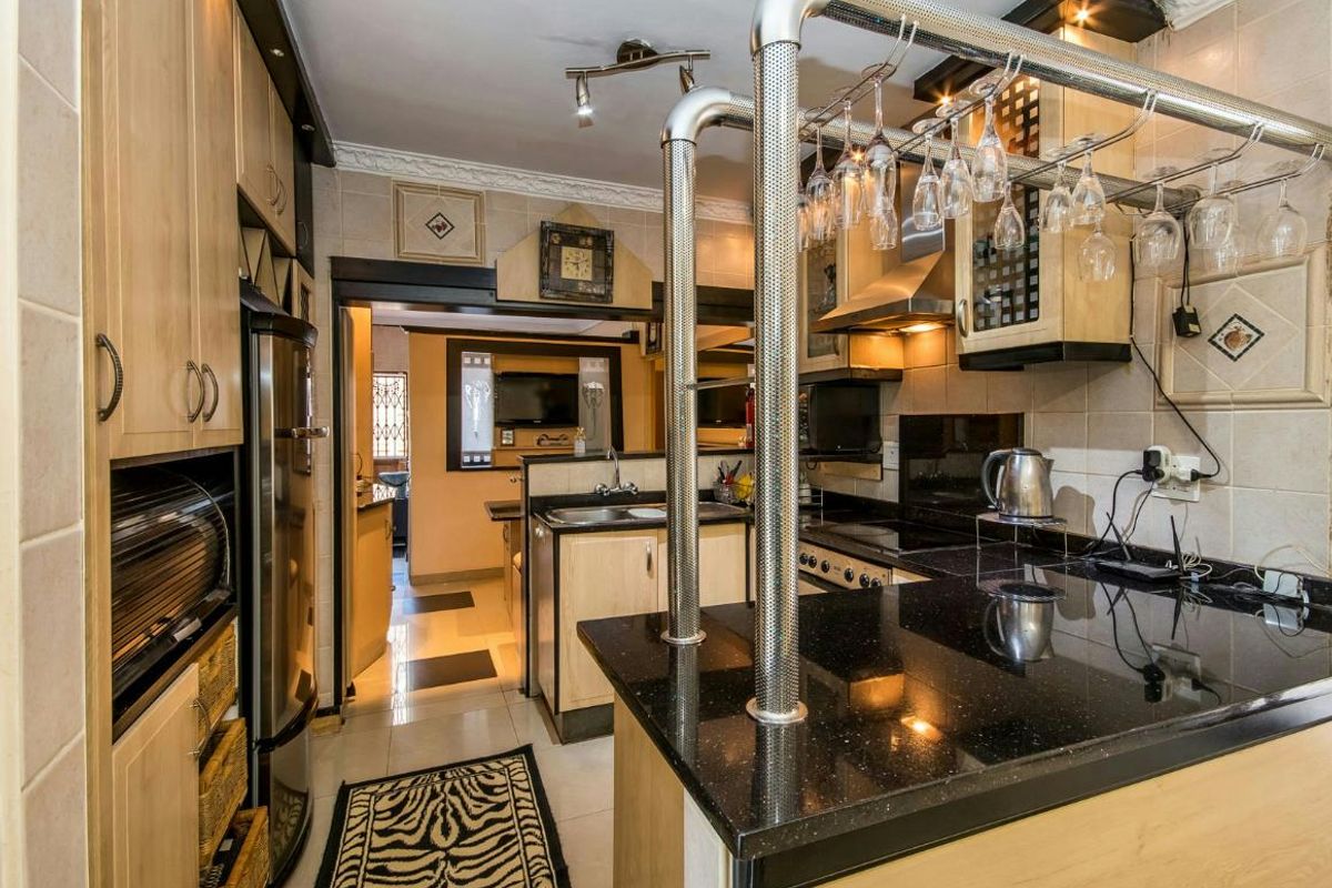 A functional kitchen featuring light wood cabinetry, dark granite countertops, built-in appliances, and a breakfast bar with overhead glass storage.