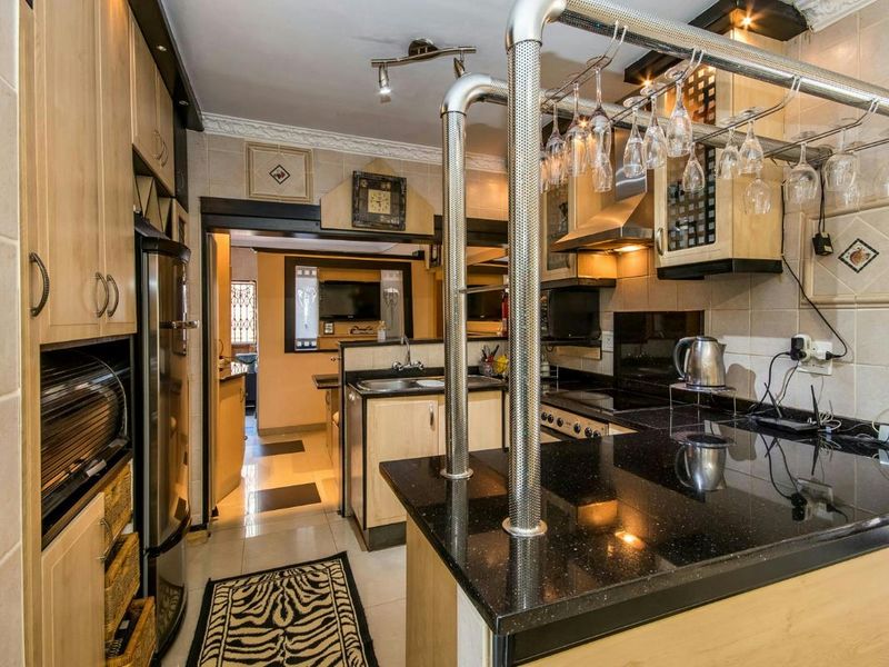 A functional kitchen featuring light wood cabinetry, dark granite countertops, built-in appliances, and a breakfast bar with overhead glass storage.