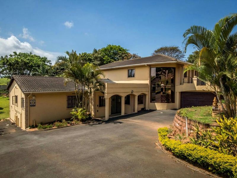 A well-maintained double-story residential property featuring a paved driveway, arched entrance, and a prominent full-height glass window facade.