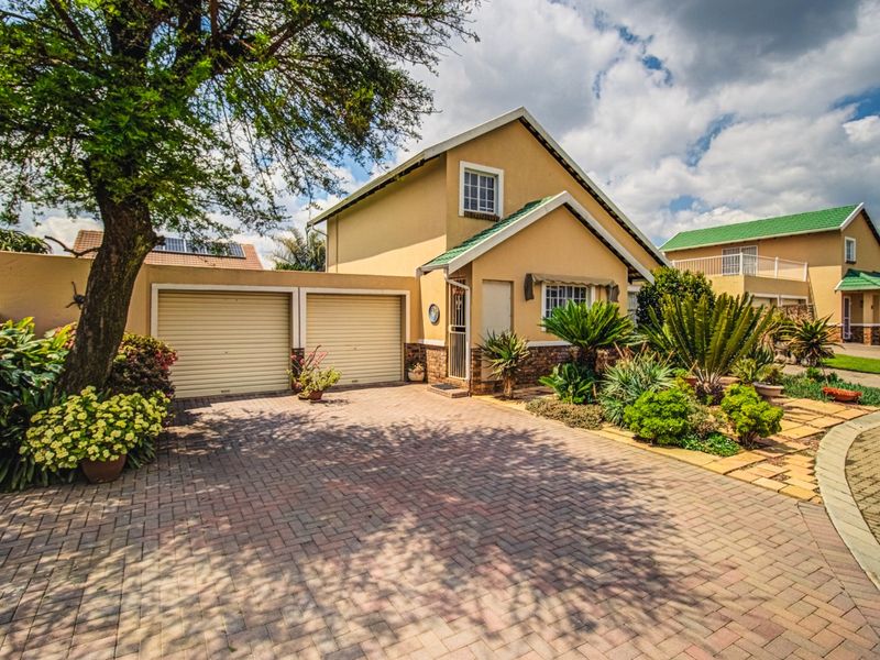Front view of a well-maintained house featuring a double garage, paved driveway, and established garden.
