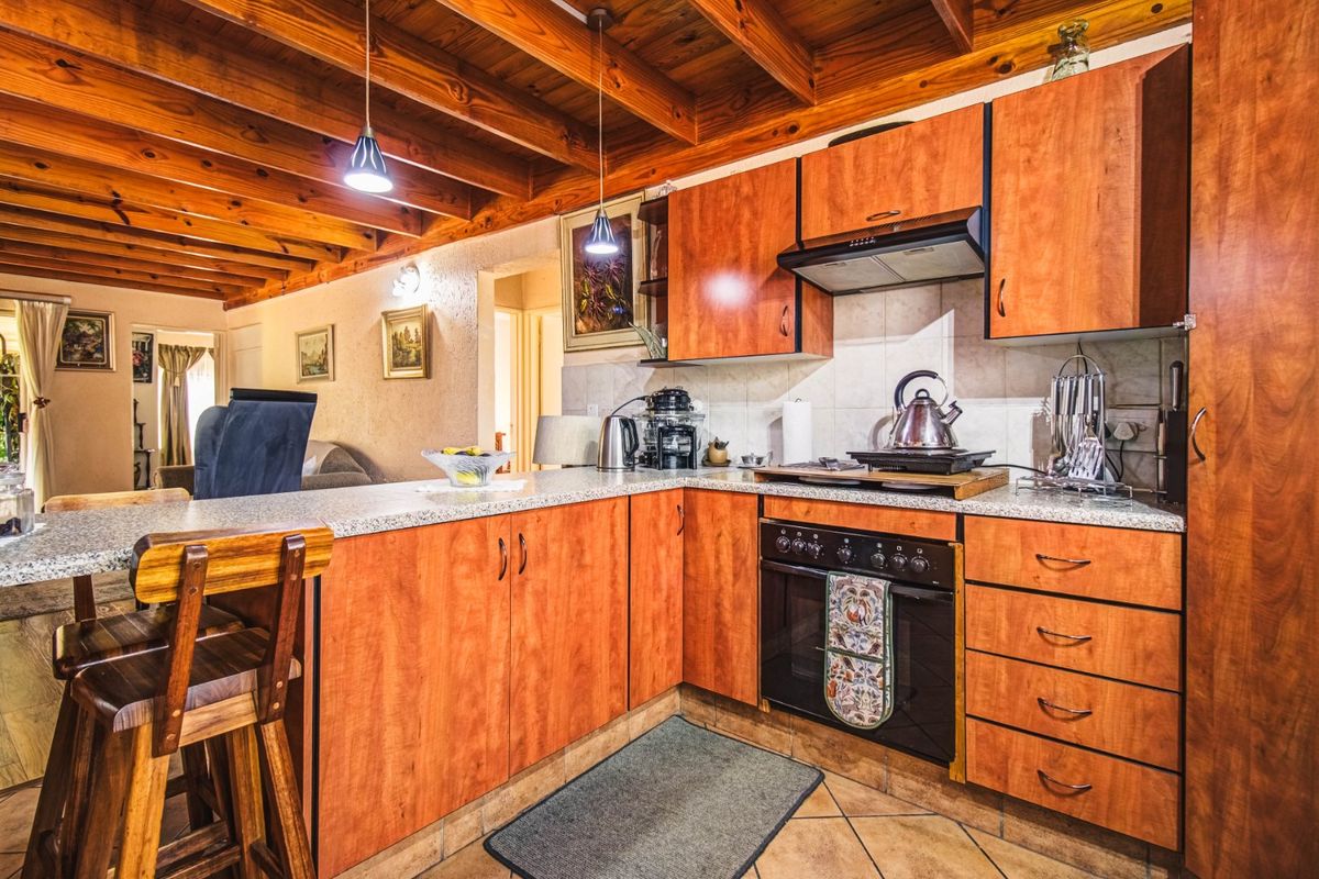 A functional kitchen featuring warm wooden exposed beam ceilings, laminate cabinetry, granite countertops, and a breakfast bar, seamlessly connected to the living area.