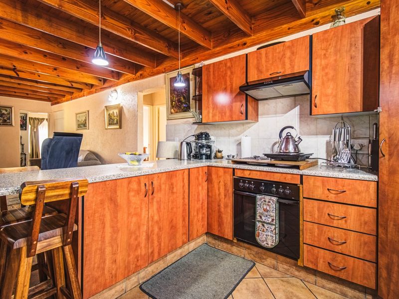 A functional kitchen featuring warm wooden exposed beam ceilings, laminate cabinetry, granite countertops, and a breakfast bar, seamlessly connected to the living area.