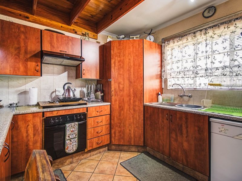 A functional kitchen featuring warm-toned wooden cabinetry, granite-look laminate countertops, a built-in oven with extractor, and exposed wooden ceiling beams.