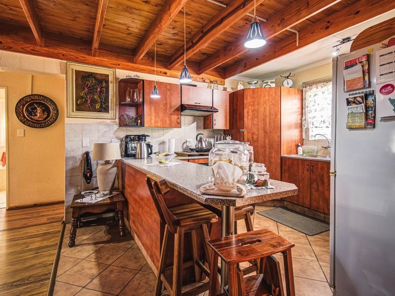 A rustic kitchen featuring exposed timber ceiling beams, warm-toned wooden cabinetry, a breakfast bar, and tiled flooring, offering a cozy and functional cooking space.
