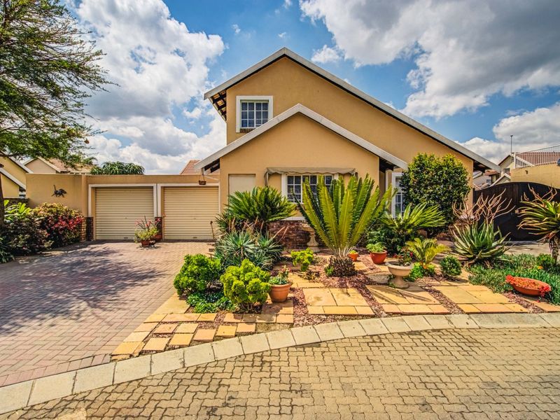 A well-maintained double-story residential home featuring a paved driveway, double garage, and established front garden with mature landscaping.