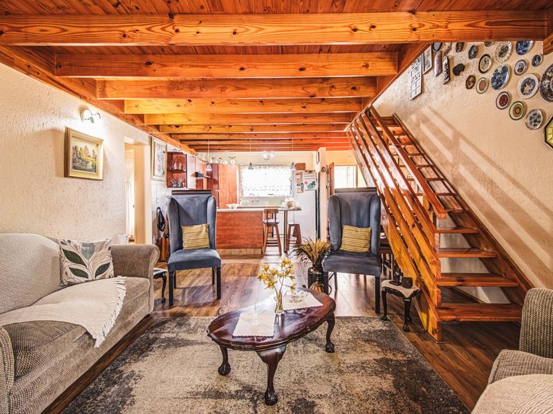 Open-plan living area featuring exposed timber ceiling beams, a wooden staircase, and integrated kitchen space with warm, rustic finishes.