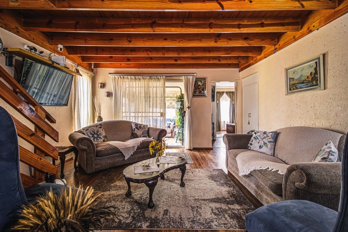 A cozy living room featuring exposed timber ceiling beams, hardwood flooring, and a staircase, with direct access to an outdoor patio area.
