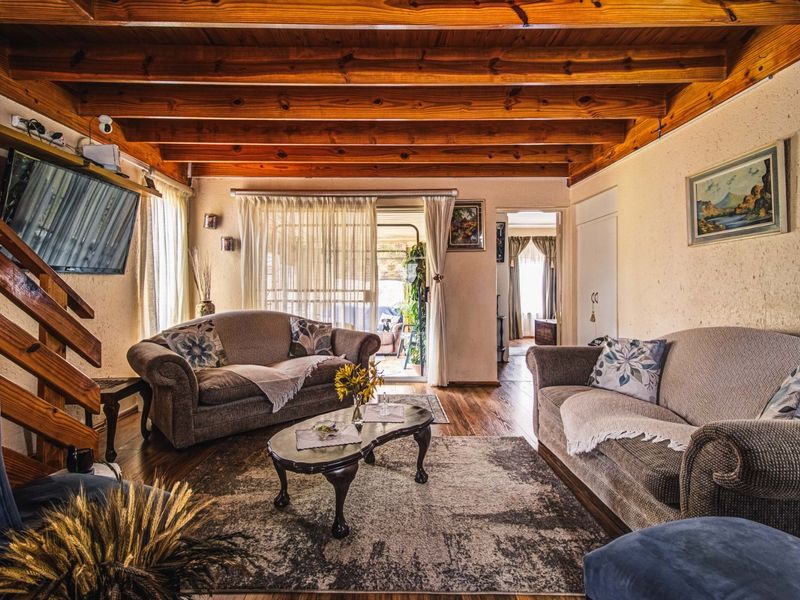 A cozy living room featuring exposed timber ceiling beams, hardwood flooring, and a staircase, with direct access to an outdoor patio area.