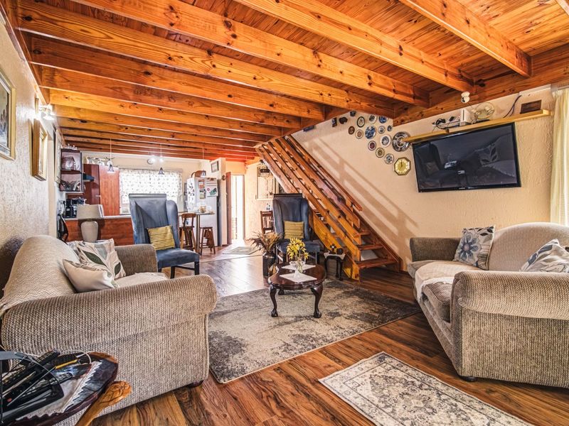 Open plan living area featuring exposed timber ceiling beams, wooden staircase, and laminate flooring, flowing into a functional kitchen space.