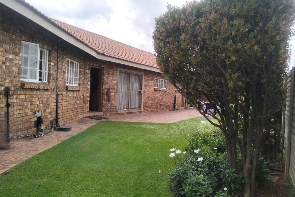 A well-maintained rear exterior view featuring a face brick facade, tiled roof, paved patio area, and a neat landscaped garden.