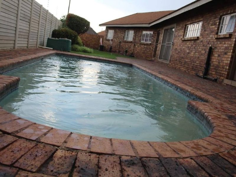 Outdoor pool area featuring a brick-paved surround, face brick house exterior, and perimeter walling.