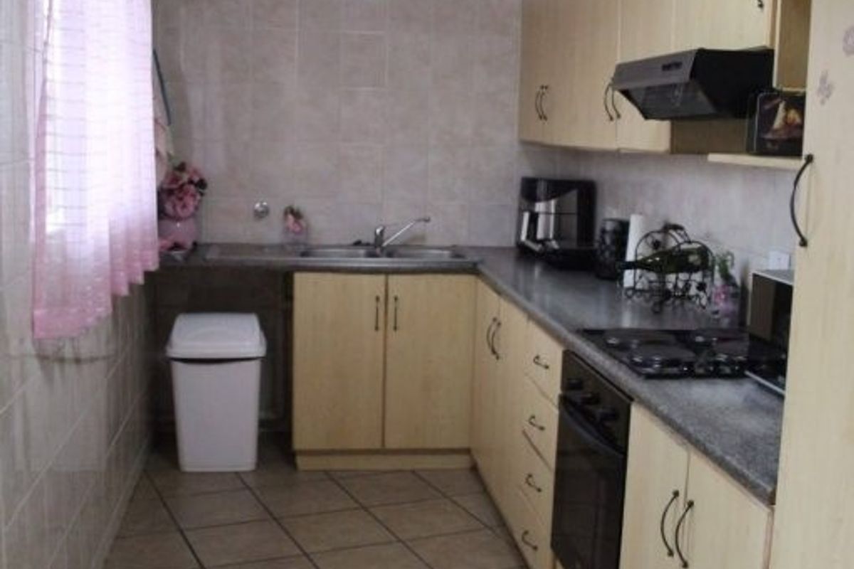 A functional kitchen featuring light-toned cabinetry, tiled walls, tiled flooring, and integrated appliances including an oven, hob, and extractor fan.