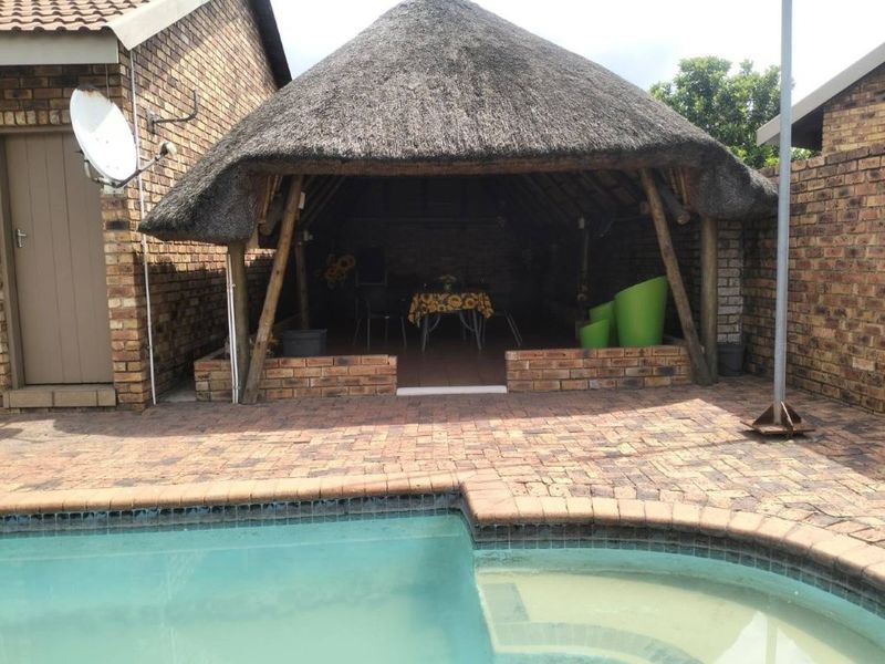 Outdoor entertainment area featuring a traditional thatched lapa structure, brick paving, and an adjacent swimming pool in a private backyard setting.