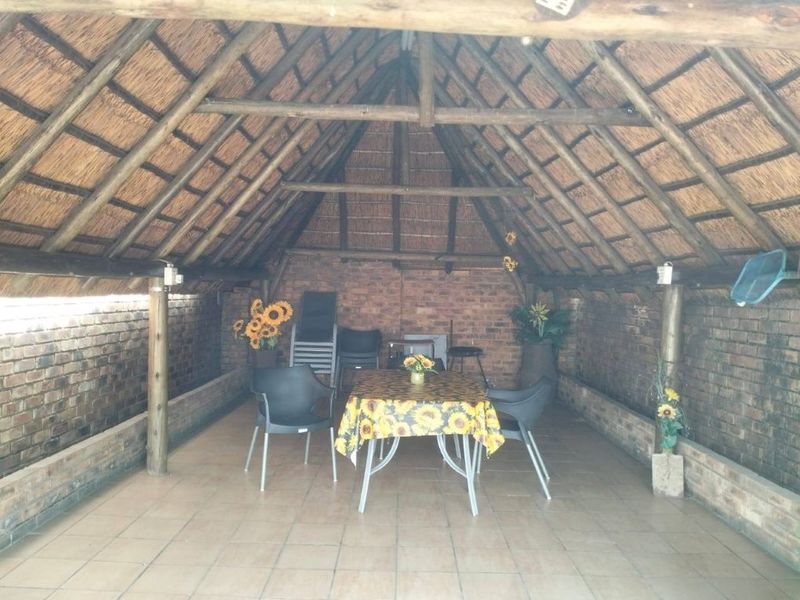 A covered outdoor patio area featuring a traditional thatched roof, exposed brick walls, and tiled flooring, providing a rustic space for outdoor dining.