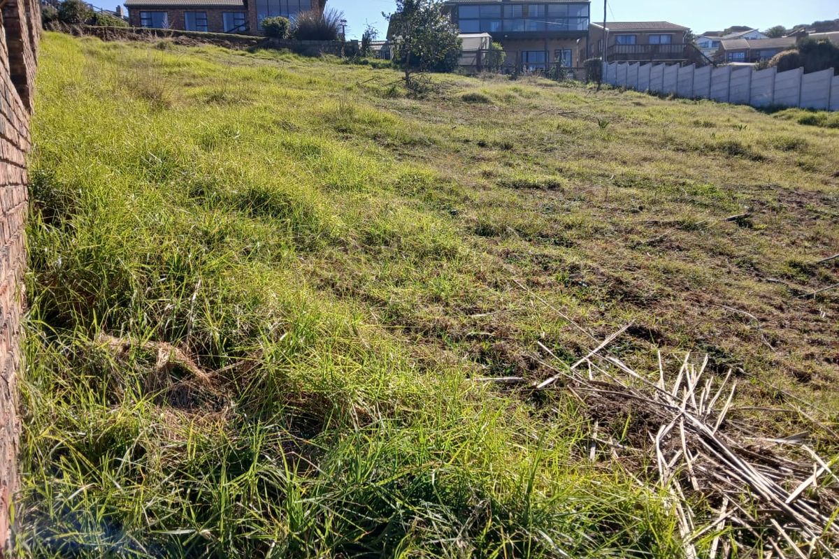 A view of a sloped, undeveloped residential plot featuring natural grass cover and a precast concrete boundary wall.