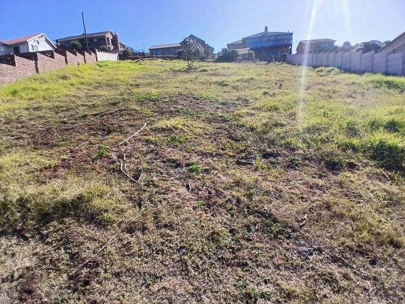 A vacant residential plot featuring a sloped landscape, enclosed by boundary walls, situated in an established neighborhood.