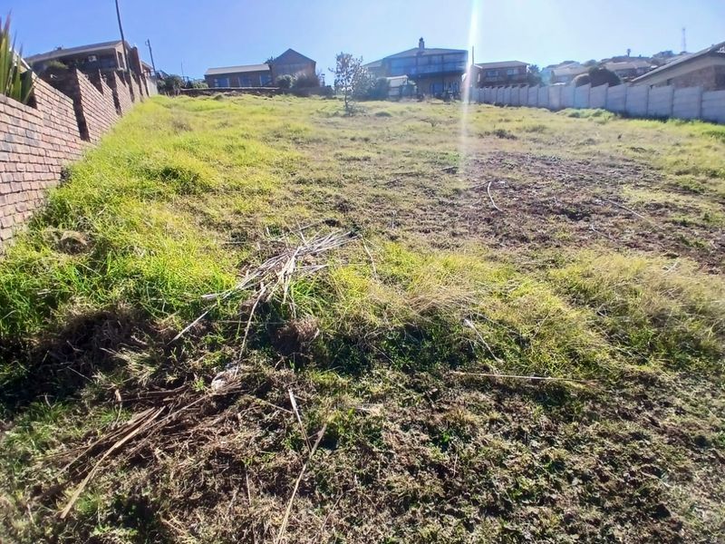A vacant residential plot featuring a sloped landscape, enclosed by brick and precast concrete boundary walls in a developed neighborhood.