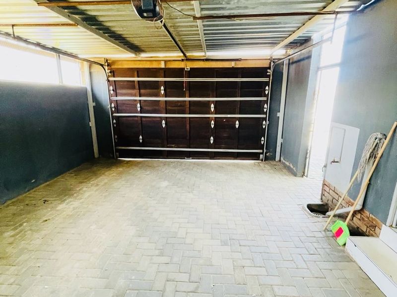 A spacious, empty garage featuring paved flooring, a sectional garage door, and a utility sink area.