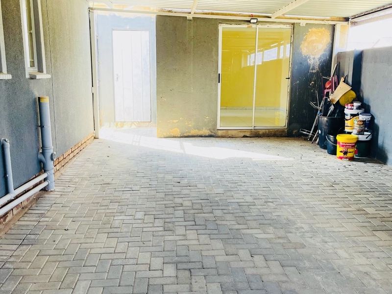 A covered outdoor patio area featuring paved flooring, a corrugated metal roof, and access to the interior via a sliding glass door.