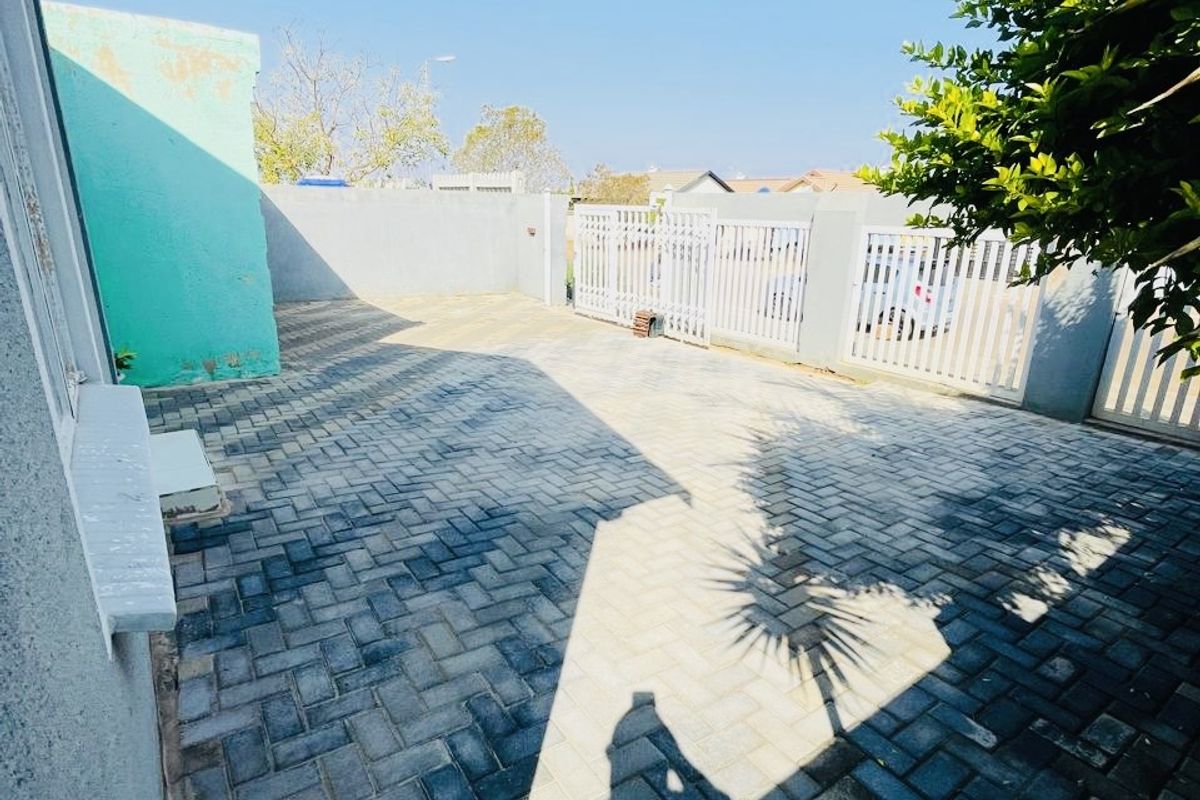 A paved rear courtyard area featuring a boundary wall and metal gate access, providing a functional outdoor space.