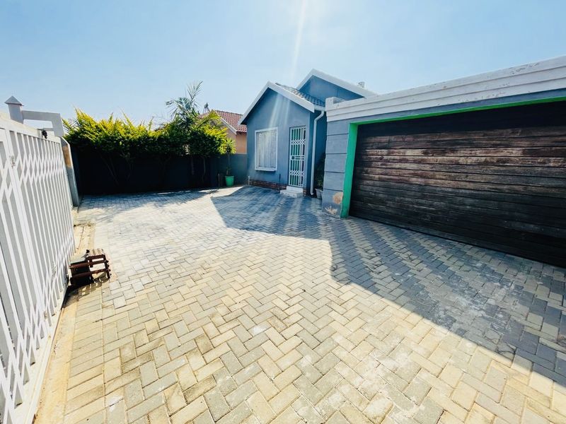 Front exterior view of the property featuring a paved driveway, secure garage access, and perimeter boundary walls.