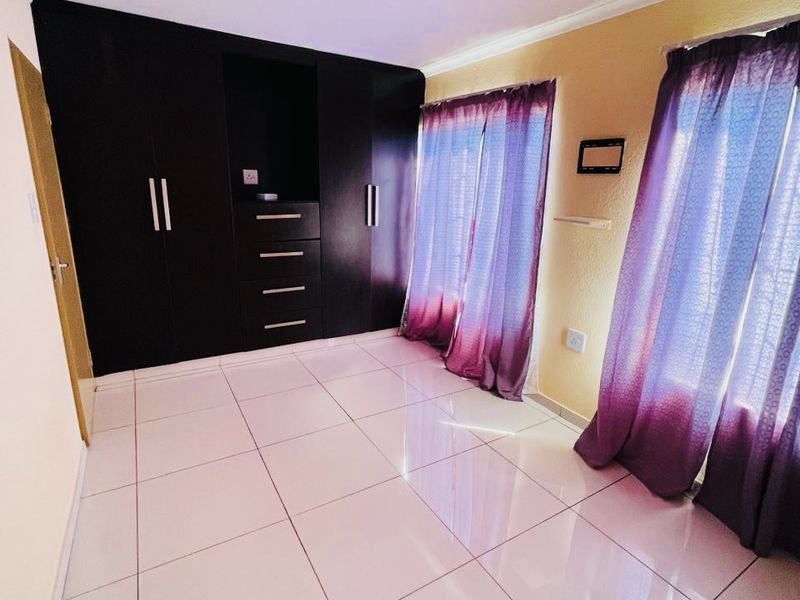 A bright, empty bedroom featuring modern tiled flooring and dark built-in cupboards with integrated shelving.