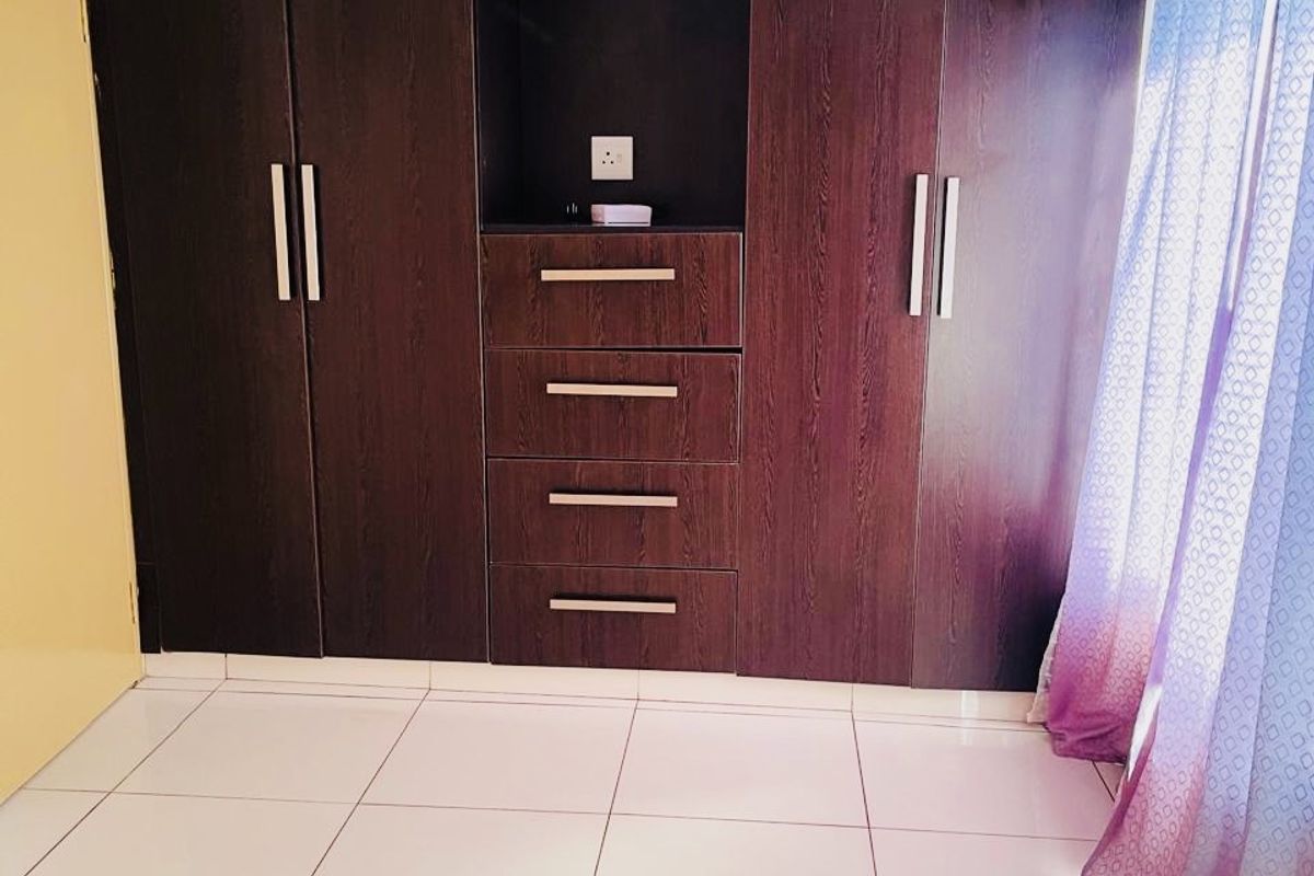 A clean bedroom featuring dark wood built-in cupboards with integrated drawers and light-colored floor tiles.