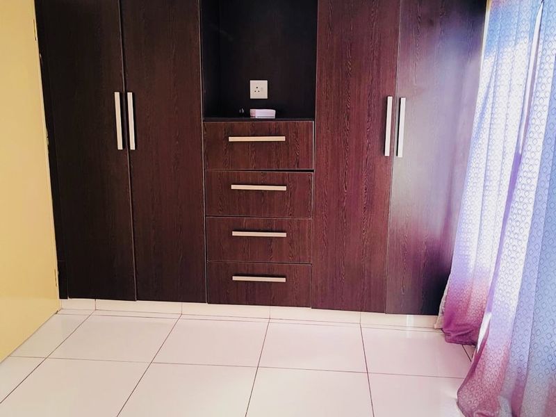 A clean bedroom featuring dark wood built-in cupboards with integrated drawers and light-colored floor tiles.