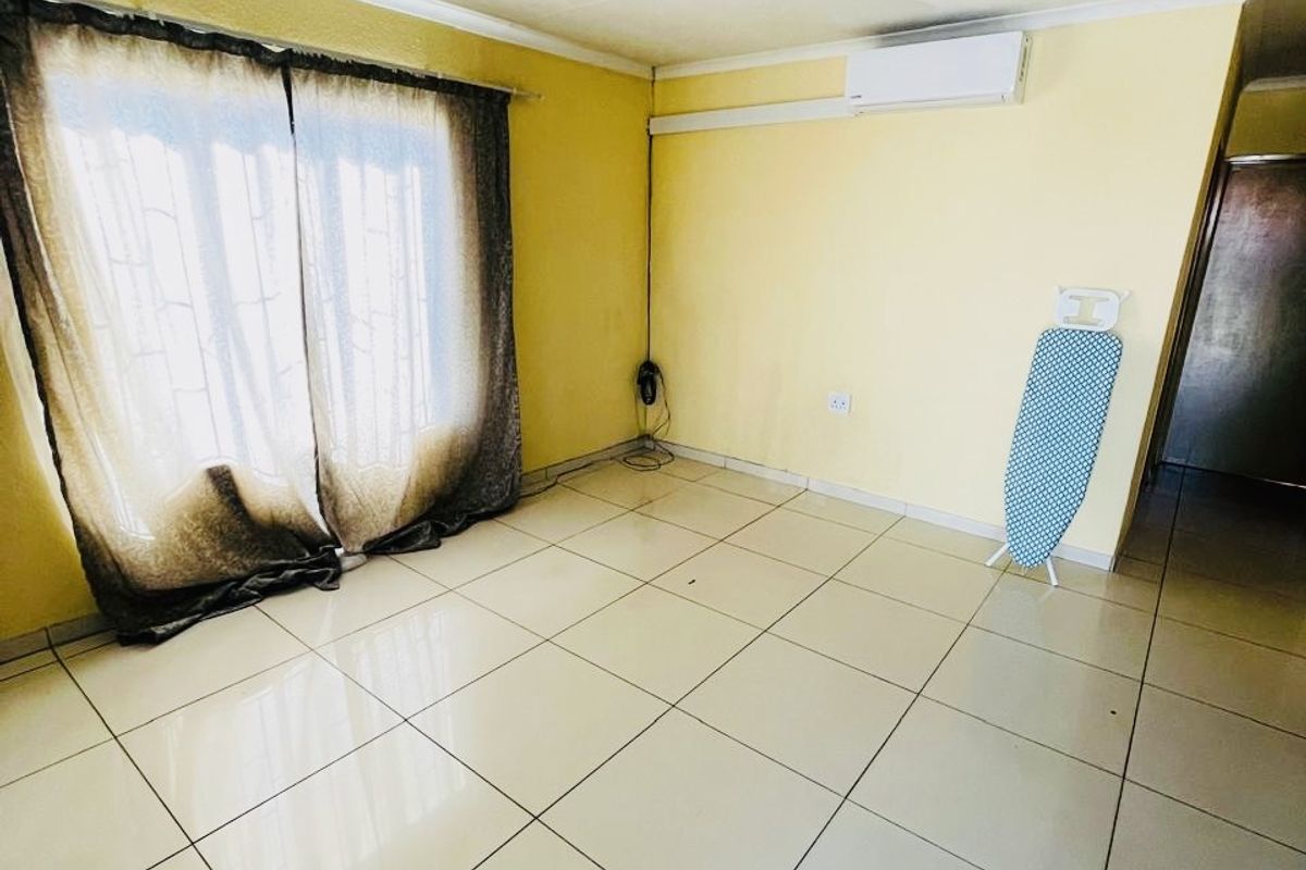 A bright, empty living room featuring large format floor tiles, a wall-mounted air conditioning unit, and sliding glass doors leading to the exterior.