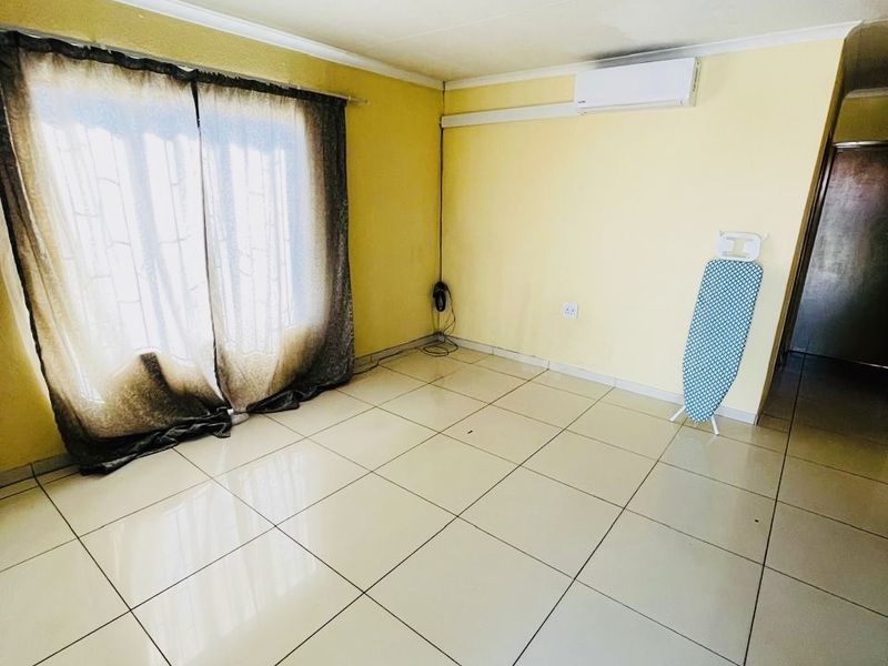 A bright, empty living room featuring large format floor tiles, a wall-mounted air conditioning unit, and sliding glass doors leading to the exterior.