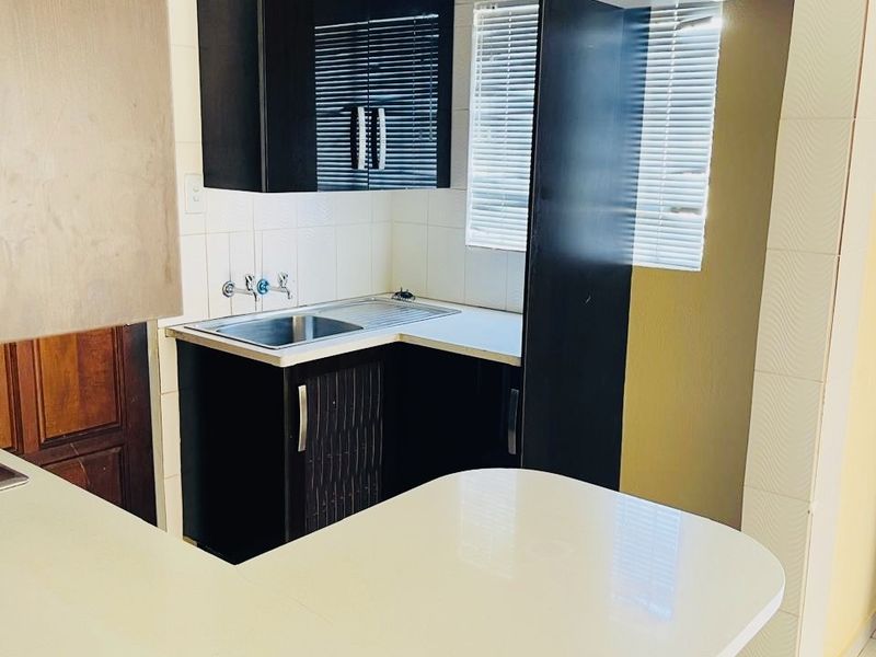 A compact kitchen featuring dark built-in cabinetry, a stainless steel sink, tiled backsplash, and a white breakfast bar counter.