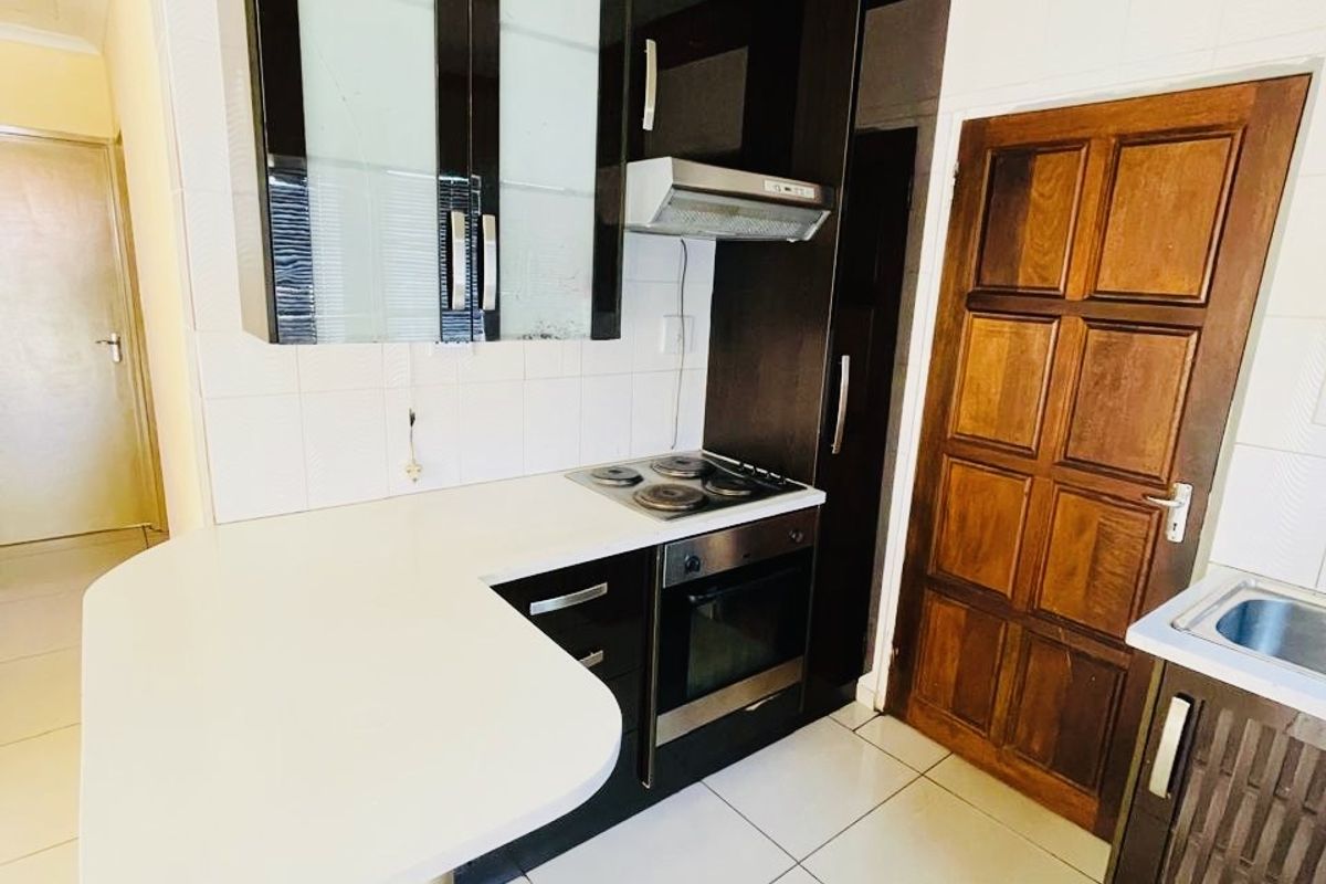 Compact kitchen featuring dark cabinetry, white countertops, a breakfast bar, built-in oven and hob, and tiled flooring.