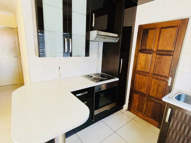 Compact kitchen featuring dark cabinetry, white countertops, a breakfast bar, built-in oven and hob, and tiled flooring.