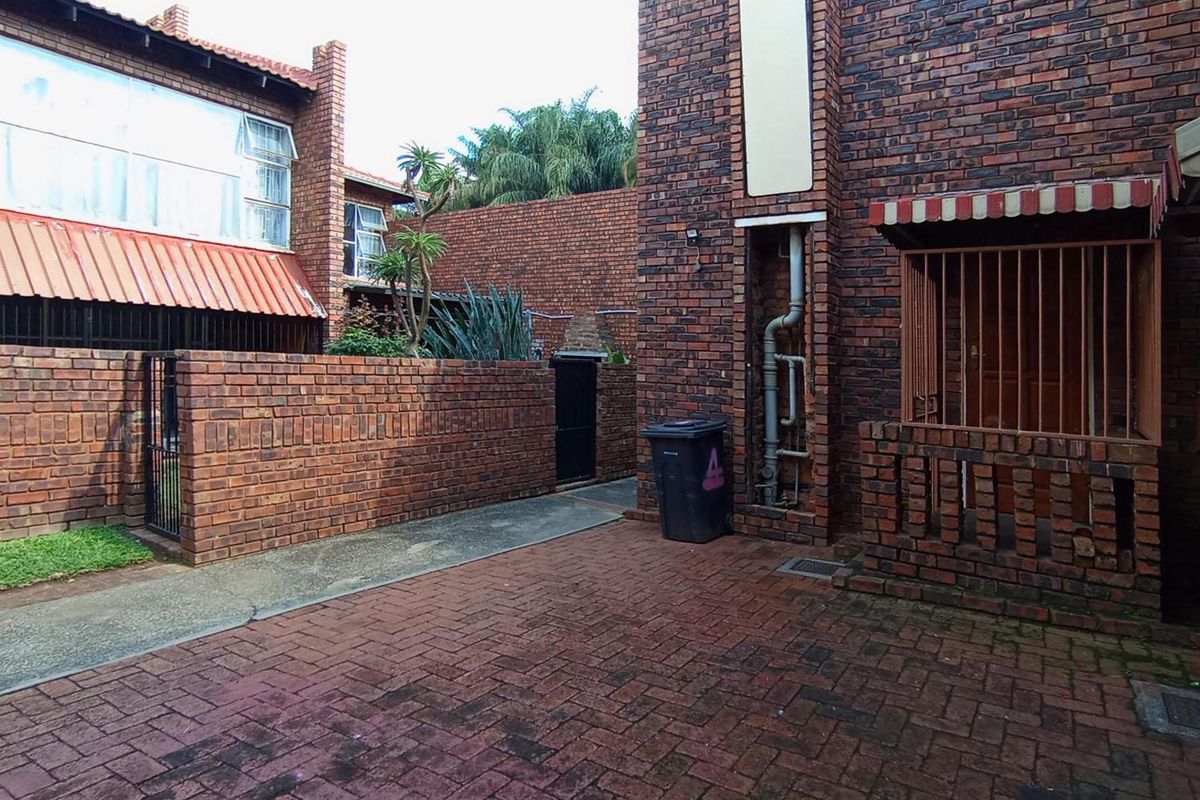 A private rear courtyard featuring face brick walls, paved flooring, and a secure entrance with an awning.