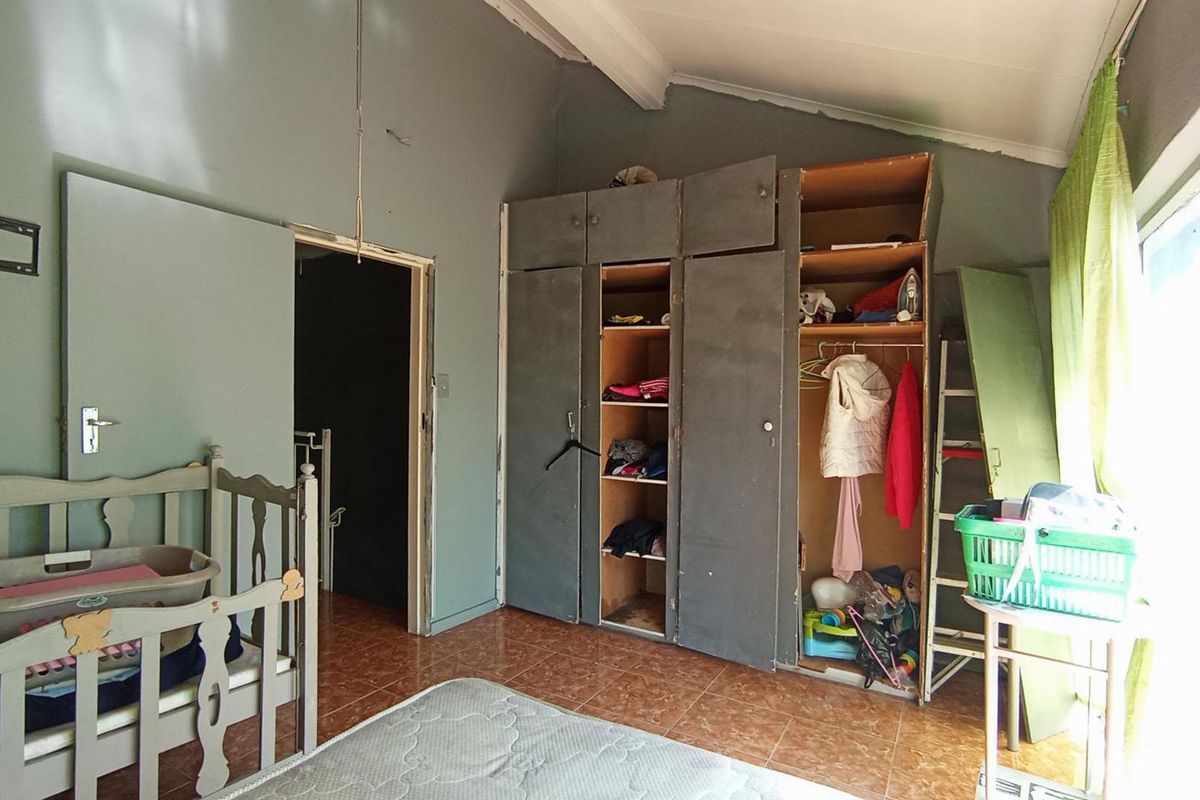 A bedroom featuring built-in cupboards, tiled flooring, and a sloped ceiling, currently requiring maintenance and cosmetic updates to improve its overall condition.